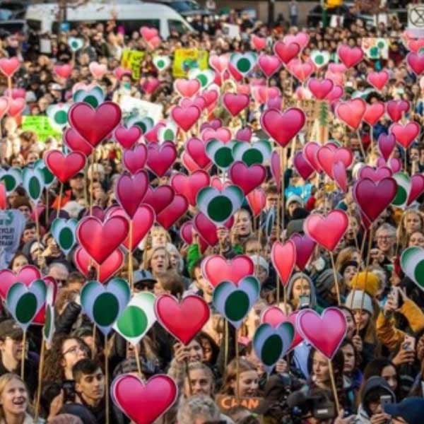 A large crowd of people holding up signs shaped like hearts.