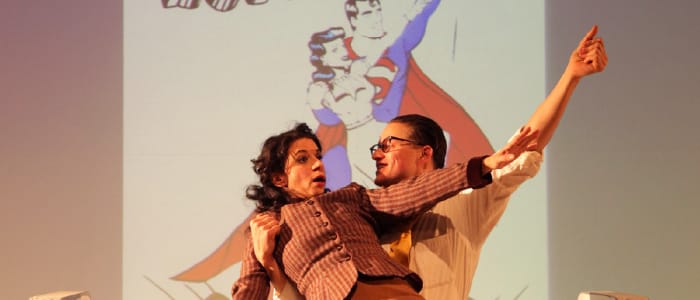 two dancing actors in front of cartoon projection of superman