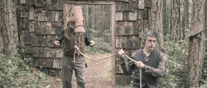 Actor Paul Ternes leading a horse puppet puppeteered by Gord Austin thru a doorway in the forest. Photo by Sophia Dagher.