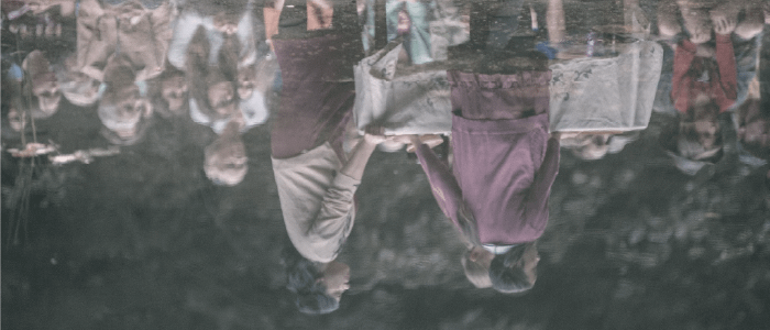 A reflection in water of actors around a table covered in a white tablecloth with audience members behind. Photo by Sophia Dagher.
